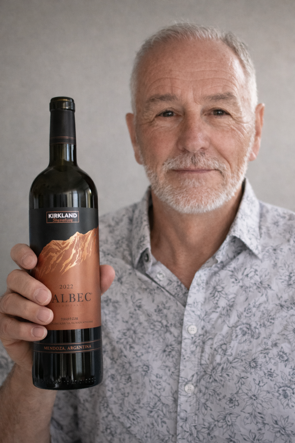 Man holding a bottle of Kirkland Signature Malbec wine, standing against a neutral background.